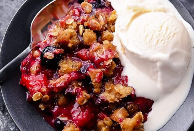 Mixed Berry Crisp with golden oat crumble topping served warm in a white baking dish with a scoop of melting vanilla ice cream, overhead shot on a rustic wooden table