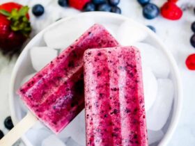 Mixed Berry Popsicles arranged on crushed ice with fresh strawberries, blueberries, and raspberries scattered around them, vibrant magenta and purple colors, bright natural lighting