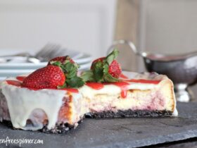 No bake cheesecake with a golden graham cracker crust, topped with fresh strawberries and a glossy berry glaze on a white marble surface