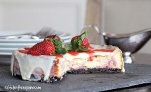 No bake cheesecake with a golden graham cracker crust, topped with fresh strawberries and a glossy berry glaze on a white marble surface
