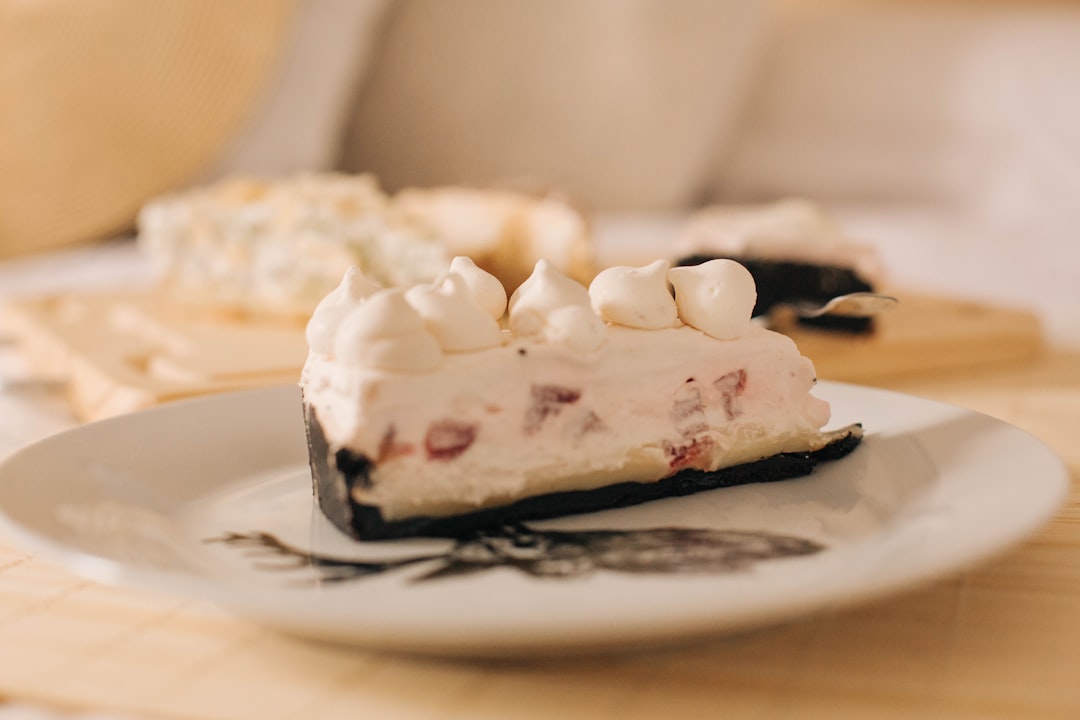 Close-up of a no bake cheesecake slice on a white plate, showing layers of buttery graham cracker crust and thick creamy filling topped with fresh raspberries and blueberries