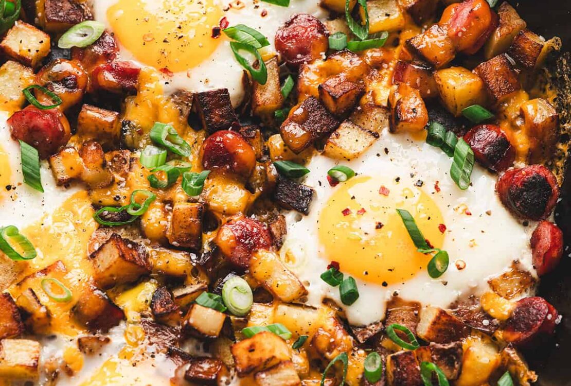 One pan camping breakfast skillet with eggs, crispy potatoes, colorful peppers, and sausage in a cast iron skillet, overhead shot, rustic wooden camp table