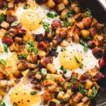 One pan camping breakfast skillet with eggs, crispy potatoes, colorful peppers, and sausage in a cast iron skillet, overhead shot, rustic wooden camp table