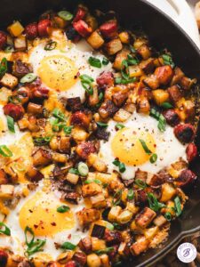 One pan camping breakfast skillet with eggs, crispy potatoes, colorful peppers, and sausage in a cast iron skillet, overhead shot, rustic wooden camp table