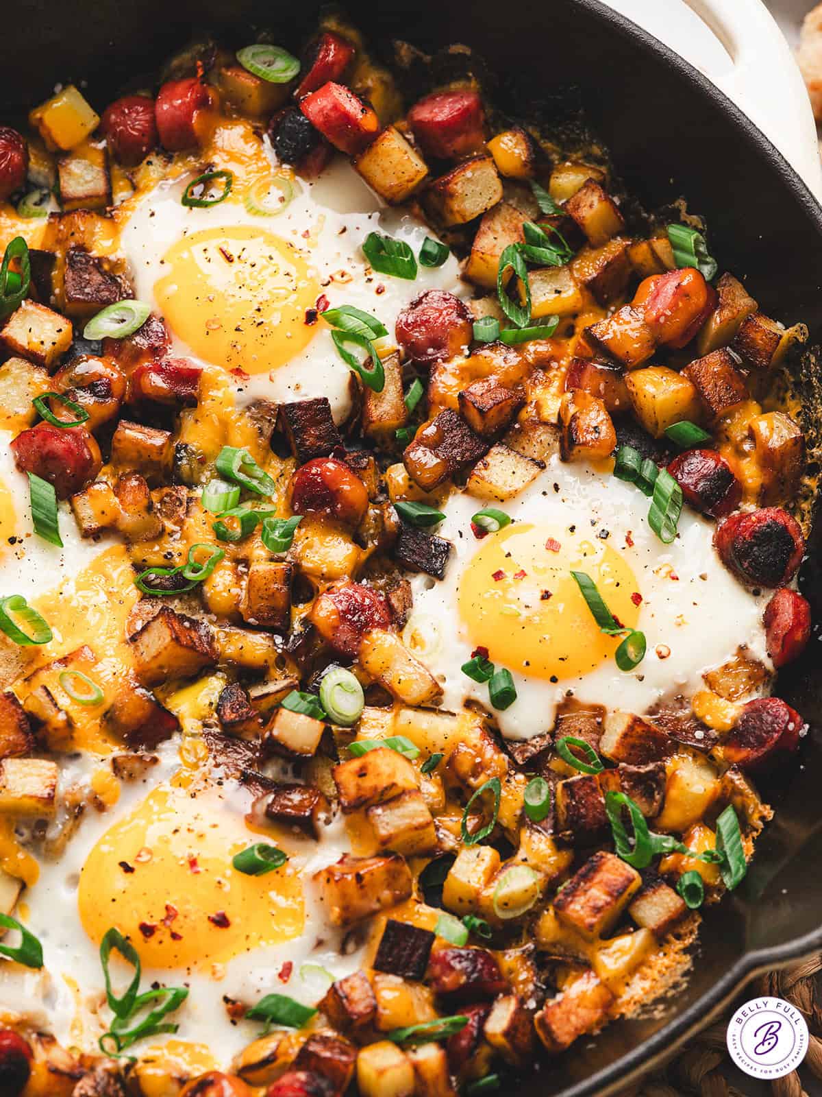 One pan camping breakfast skillet with eggs, crispy potatoes, colorful peppers, and sausage in a cast iron skillet, overhead shot, rustic wooden camp table