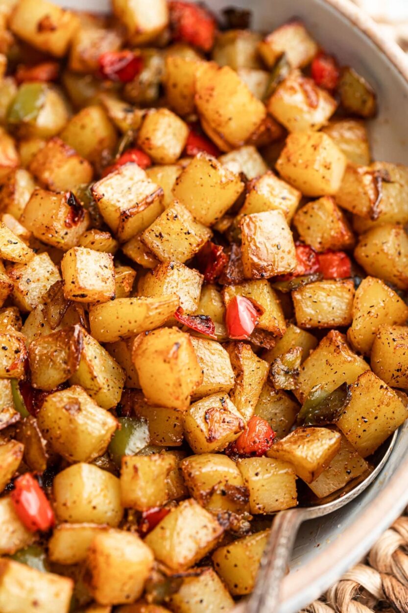 Cast iron skillet with diced potatoes browning in sausage fat, colorful bell peppers and onions being added, step-by-step process shot from above