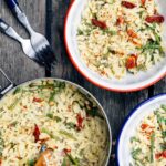 One pot cheesy orzo with asparagus served in a wide shallow bowl, creamy and golden with bright green asparagus and freshly grated Parmesan on top, photographed overhead on a rustic wooden table with a linen napkin and fork
