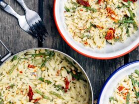 One pot cheesy orzo with asparagus served in a wide shallow bowl, creamy and golden with bright green asparagus and freshly grated Parmesan on top, photographed overhead on a rustic wooden table with a linen napkin and fork