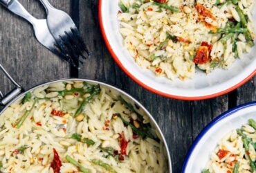 One pot cheesy orzo with asparagus served in a wide shallow bowl, creamy and golden with bright green asparagus and freshly grated Parmesan on top, photographed overhead on a rustic wooden table with a linen napkin and fork