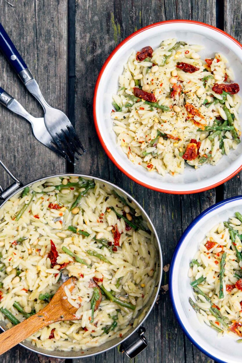 Close-up shot of one pot cheesy orzo with asparagus in the pot, steam rising, with a wooden spoon pulling through to show the creamy, stretchy cheese sauce coating the orzo and bright green asparagus pieces, golden Parmesan crust forming at edges