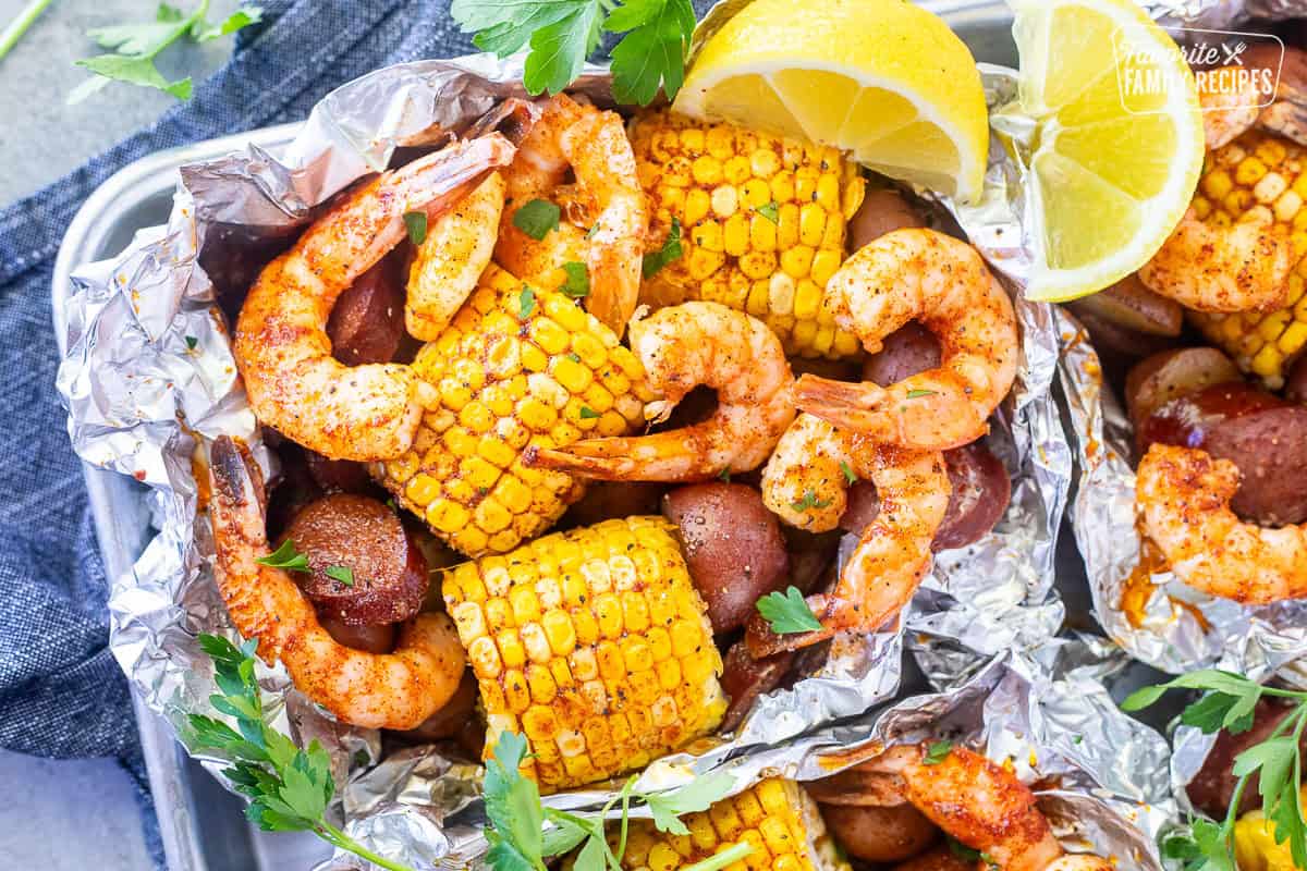 overhead flat lay of shrimp boil foil packet ingredients laid out on a wooden surface — raw shrimp, sausage slices, corn rounds, baby potatoes, garlic butter, and Cajun seasoning
