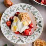 Classic strawberry shortcake with flaky golden biscuits, macerated strawberries and syrup, and billowy whipped cream on a white plate