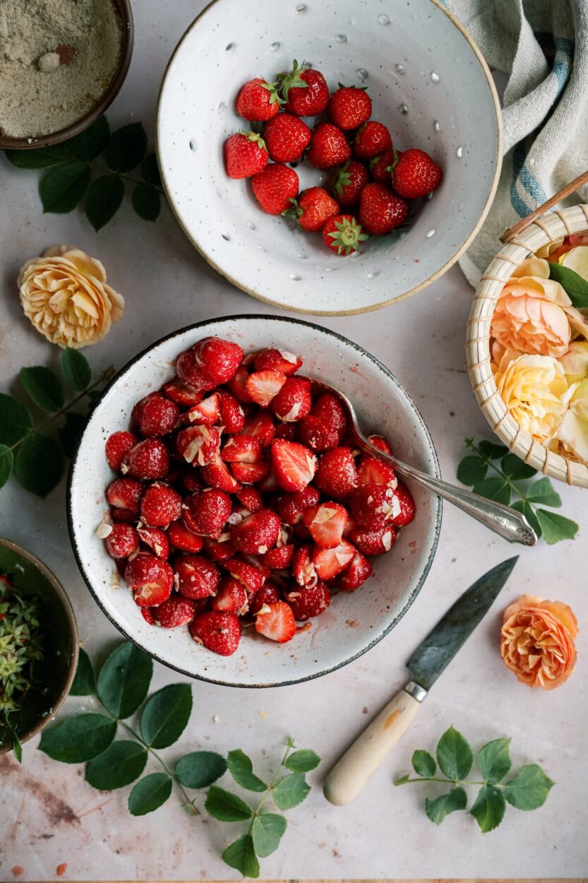 Step-by-step shot showing cold butter being cut into flour for shortcake biscuit dough alongside macerated strawberries in a bowl