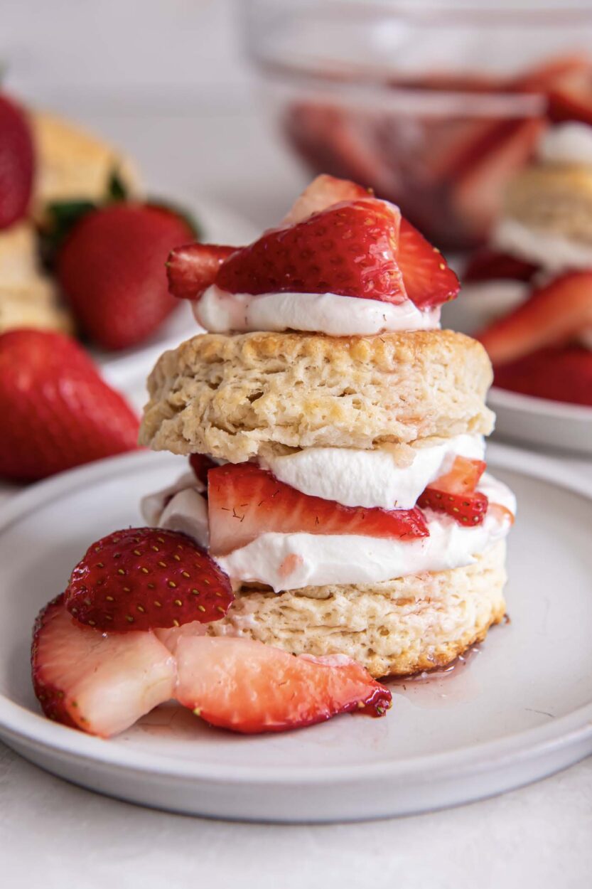 Close-up of strawberry shortcake showing layers of flaky biscuit soaked with berry syrup and a generous cloud of vanilla whipped cream with fresh strawberry slices on top