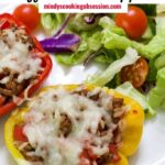 Stuffed bell peppers filled with cheesy ground beef and rice, golden melted cheese on top, plated on a white dish with fresh herbs