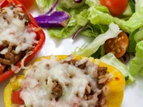 Stuffed bell peppers filled with cheesy ground beef and rice, golden melted cheese on top, plated on a white dish with fresh herbs