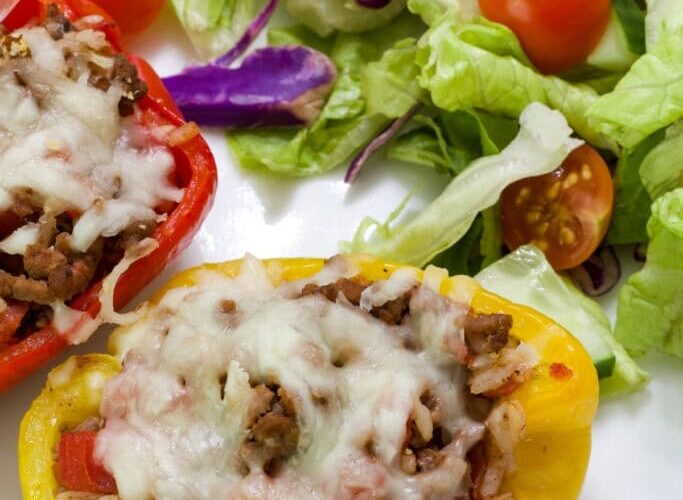 Stuffed bell peppers filled with cheesy ground beef and rice, golden melted cheese on top, plated on a white dish with fresh herbs