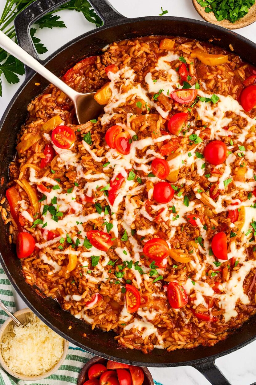 Overhead shot of halved raw bell peppers, seasoned ground beef in a skillet, cooked rice, and shredded cheese arranged on a wooden cutting board