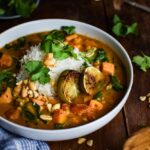 Sweet Potato Peanut Stew served in a rustic bowl with fresh cilantro, crushed peanuts, and a wedge of lime on a dark wooden table — finished dish beautifully plated