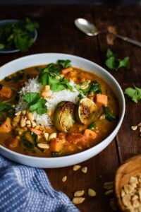 Sweet Potato Peanut Stew served in a rustic bowl with fresh cilantro, crushed peanuts, and a wedge of lime on a dark wooden table — finished dish beautifully plated