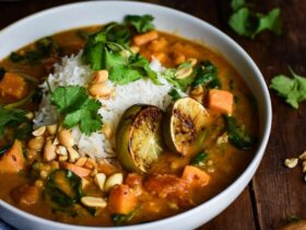 Sweet Potato Peanut Stew served in a rustic bowl with fresh cilantro, crushed peanuts, and a wedge of lime on a dark wooden table — finished dish beautifully plated