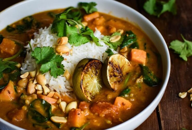 Sweet Potato Peanut Stew served in a rustic bowl with fresh cilantro, crushed peanuts, and a wedge of lime on a dark wooden table — finished dish beautifully plated