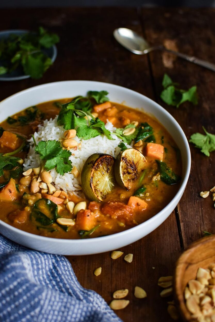 Sweet Potato Peanut Stew served in a rustic bowl with fresh cilantro, crushed peanuts, and a wedge of lime on a dark wooden table — finished dish beautifully plated