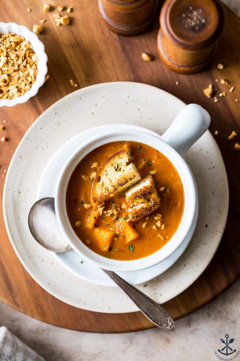 Close-up of Sweet Potato Peanut Stew in a deep bowl, showing the glossy peanut sauce coating chunks of sweet potato and chickpeas, garnished with chopped peanuts, fresh cilantro, and a squeeze of lime
