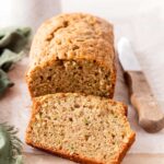 Sliced zucchini bread loaf with golden crust on a wooden cutting board, dusted with cinnamon sugar, warm and moist crumb visible