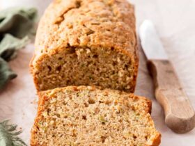 Sliced zucchini bread loaf with golden crust on a wooden cutting board, dusted with cinnamon sugar, warm and moist crumb visible
