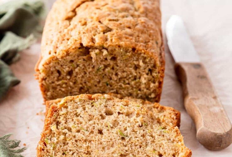 Sliced zucchini bread loaf with golden crust on a wooden cutting board, dusted with cinnamon sugar, warm and moist crumb visible
