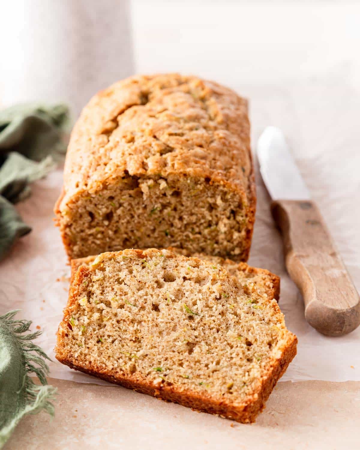 Sliced zucchini bread loaf with golden crust on a wooden cutting board, dusted with cinnamon sugar, warm and moist crumb visible
