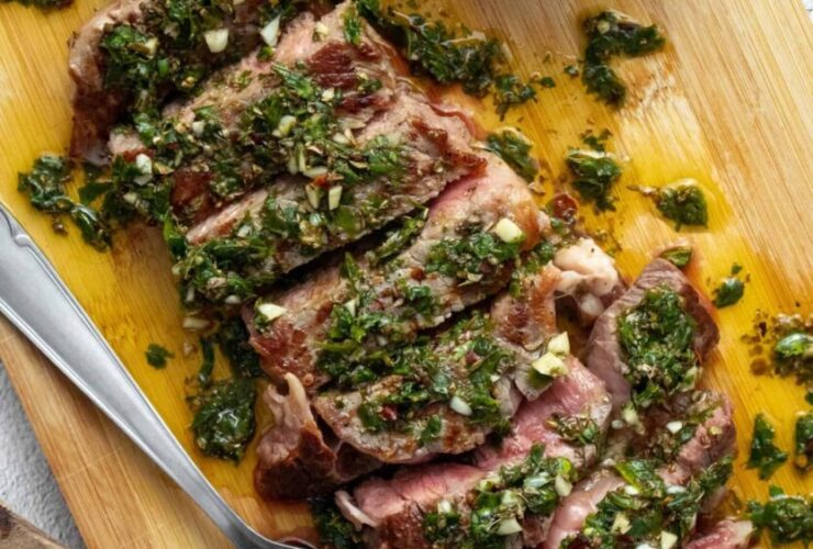 Argentinian chimichurri steak sliced and plated with vibrant green herb sauce drizzled over the top, served on a dark wooden board with grilled char marks visible