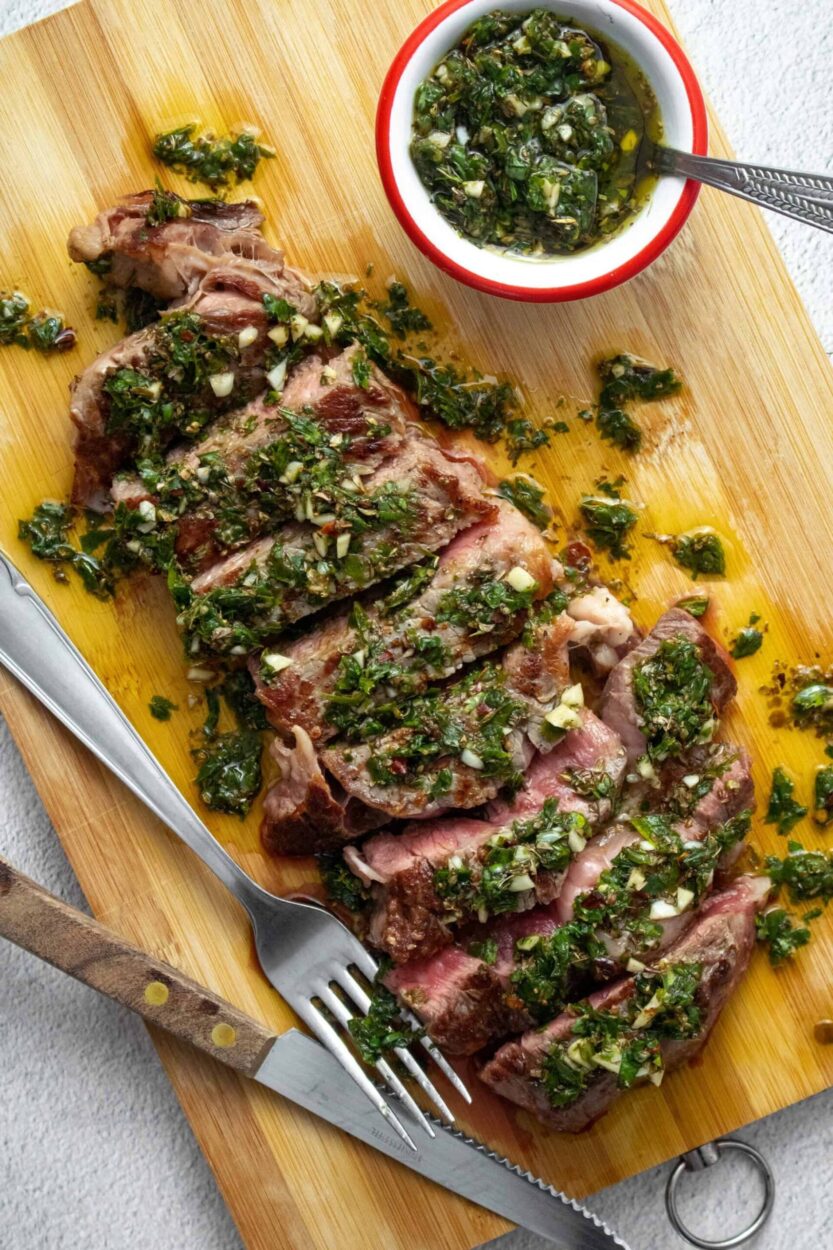 Argentinian chimichurri steak sliced and plated with vibrant green herb sauce drizzled over the top, served on a dark wooden board with grilled char marks visible