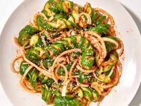 Asian cucumber noodle salad spiralized cucumber noodles in a white bowl with sesame seeds, sliced scallions, red chili, and golden sesame-ginger dressing, overhead shot on a wooden table
