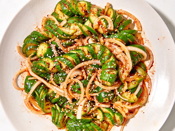 Asian cucumber noodle salad spiralized cucumber noodles in a white bowl with sesame seeds, sliced scallions, red chili, and golden sesame-ginger dressing, overhead shot on a wooden table
