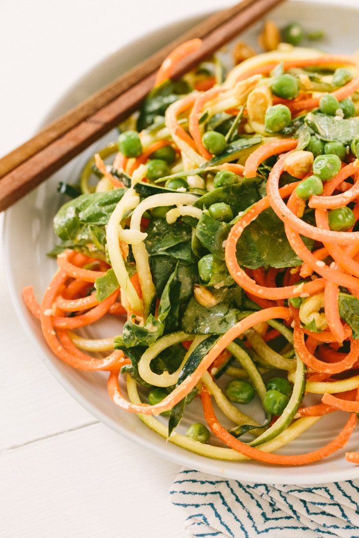 spiralized cucumber noodle salad ingredients flat lay including English cucumbers, toasted sesame oil bottle, fresh ginger root, soy sauce, rice vinegar, sesame seeds, scallions, and red chili flakes on a marble surface