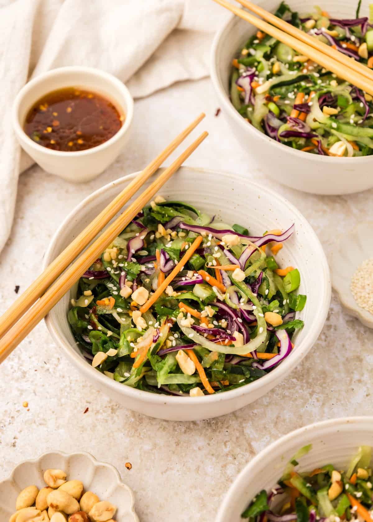 close-up of Asian cucumber noodle salad spiralized noodles in a bowl topped with toasted sesame seeds, sliced scallions, and red chili flakes with chopsticks resting on the edge