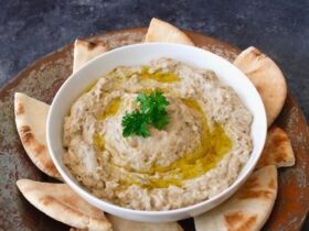 Baba Ganoush served in a wide shallow bowl drizzled with olive oil, topped with paprika, fresh parsley, and a side of warm pita bread on a rustic wooden table