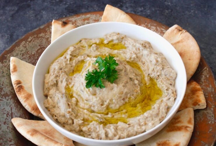 Baba Ganoush served in a wide shallow bowl drizzled with olive oil, topped with paprika, fresh parsley, and a side of warm pita bread on a rustic wooden table