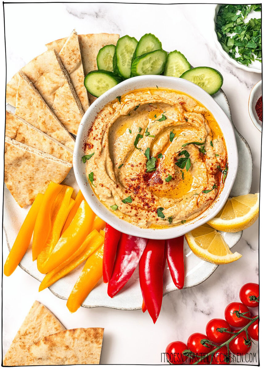 Close-up overhead shot of Baba Ganoush in a ceramic bowl with a swirl of olive oil, scattered pomegranate seeds, smoked paprika, and fresh parsley, with torn pita bread on the side ready for dipping