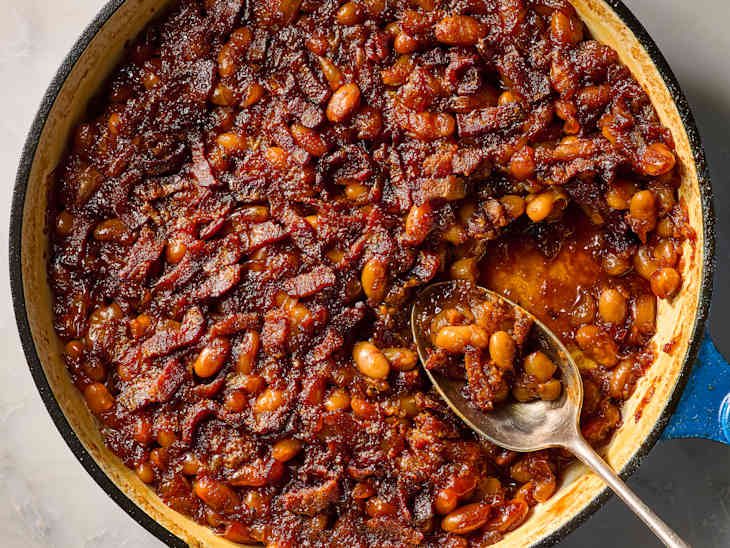 A flat lay overhead shot of all the BBQ baked beans ingredients arranged on a white marble surface — navy beans in a bowl, bacon strips, brown sugar, ketchup, mustard, apple cider vinegar, smoked paprika, and liquid smoke bottles
