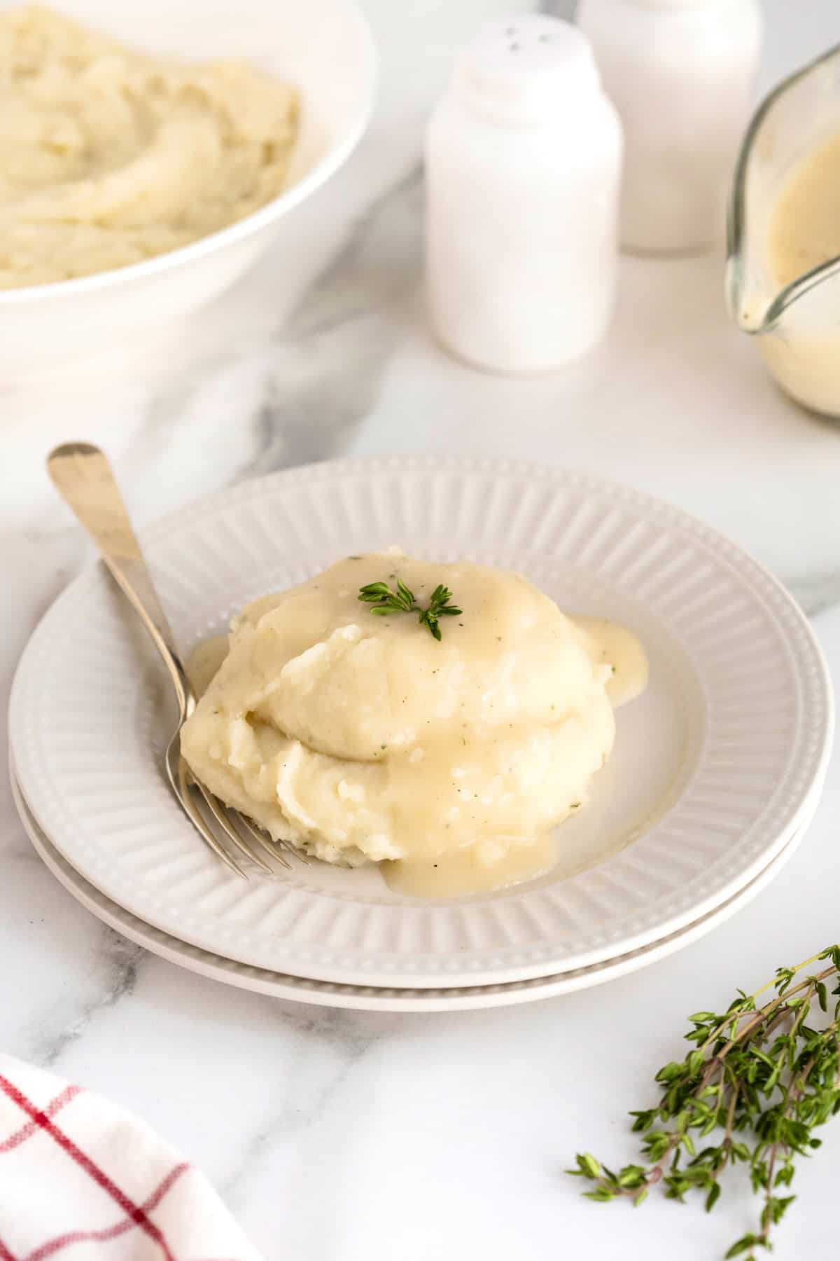 Close-up of silky brown butter turkey gravy being ladled over a generous pile of creamy mashed potatoes with flecks of thyme visible in the glossy gravy