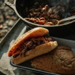 Campfire Sloppy Joes piled high on a toasted brioche bun, served on a rustic tin plate beside a glowing campfire at dusk