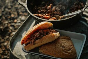Campfire Sloppy Joes piled high on a toasted brioche bun, served on a rustic tin plate beside a glowing campfire at dusk