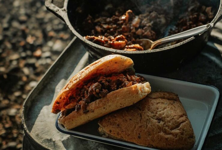 Campfire Sloppy Joes piled high on a toasted brioche bun, served on a rustic tin plate beside a glowing campfire at dusk