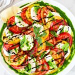 Caprese Salad beautifully plated on a white marble board with sliced ripe tomatoes, fresh mozzarella, basil leaves, and a drizzle of balsamic glaze and olive oil