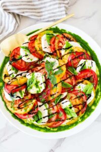 Caprese Salad beautifully plated on a white marble board with sliced ripe tomatoes, fresh mozzarella, basil leaves, and a drizzle of balsamic glaze and olive oil