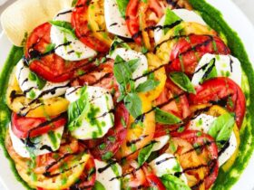 Caprese Salad beautifully plated on a white marble board with sliced ripe tomatoes, fresh mozzarella, basil leaves, and a drizzle of balsamic glaze and olive oil