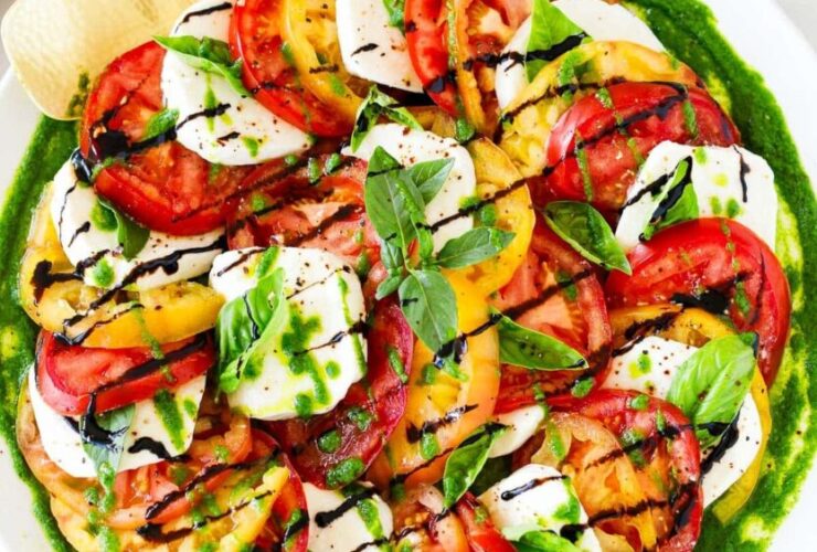 Caprese Salad beautifully plated on a white marble board with sliced ripe tomatoes, fresh mozzarella, basil leaves, and a drizzle of balsamic glaze and olive oil